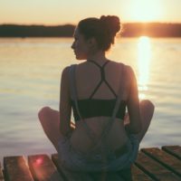 woman sitting on wooden dock during sunset