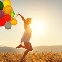 mujer feliz saltando en medio del campo llevando globos de diferentes colores