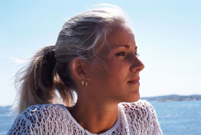 blonde woman wearing knitted top thinking near a body of water