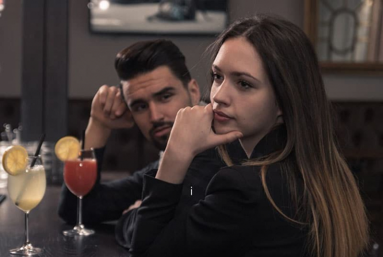 disappointed woman sitting beside a man in a bar with drinks on the table