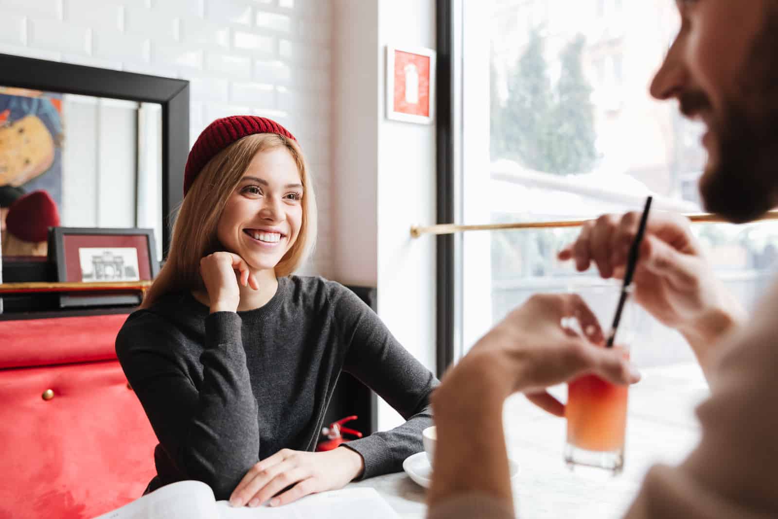 Mulher sorridente de chapéu vermelho a falar com um homem junto à mesa num café