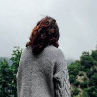 woman in gray sweater standing in forest