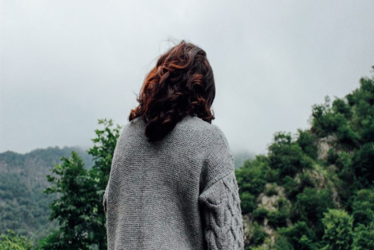 donna con maglione grigio in piedi nella foresta