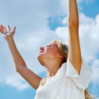 woman with arms raised smiling wearing white dress during daytime