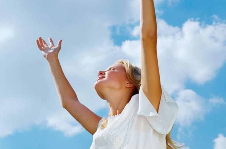 woman with arms raised smiling wearing white dress during daytime