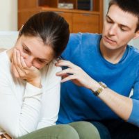 hurt woman crying sitting on sofa next to a man who's trying to calm her
