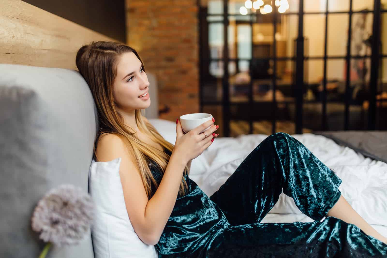 a beautiful woman is lying in bed drinking coffee