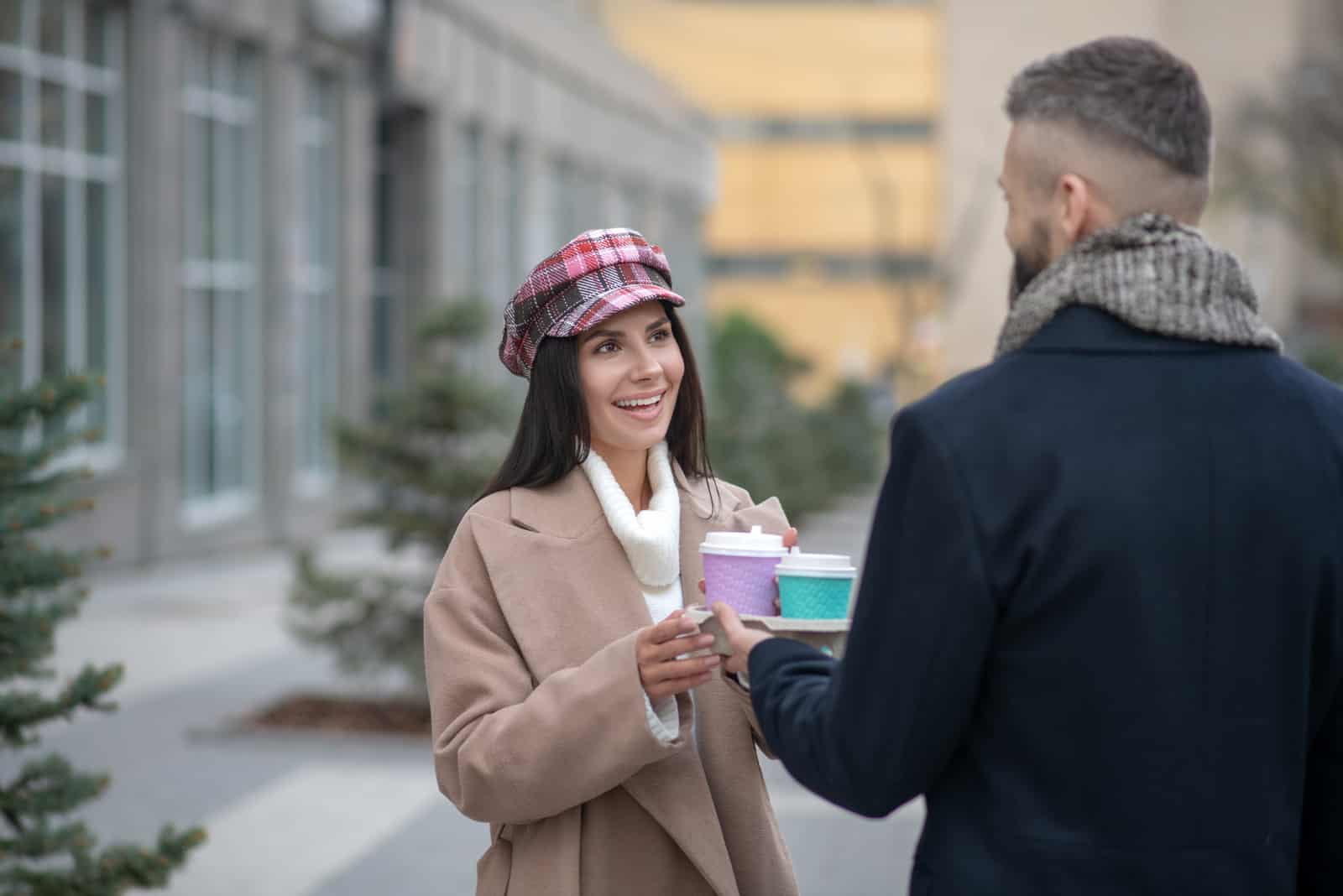 a man and a woman standing holding coffee in their hands and talking