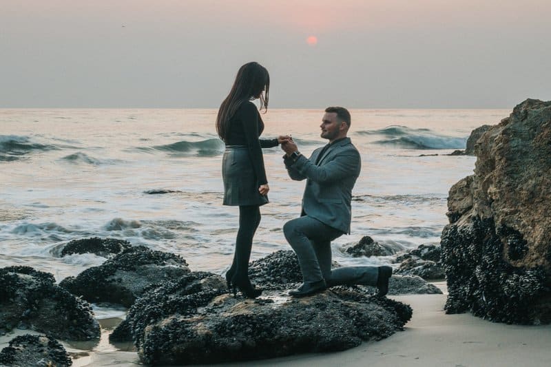 a man in a gray suit on the seashore proposes to a girl