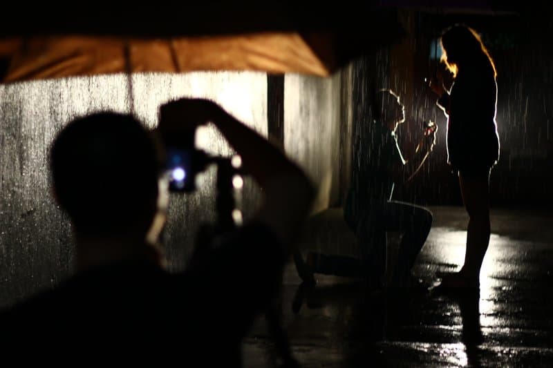 a photographer under a brown umbrella photographs a proposal