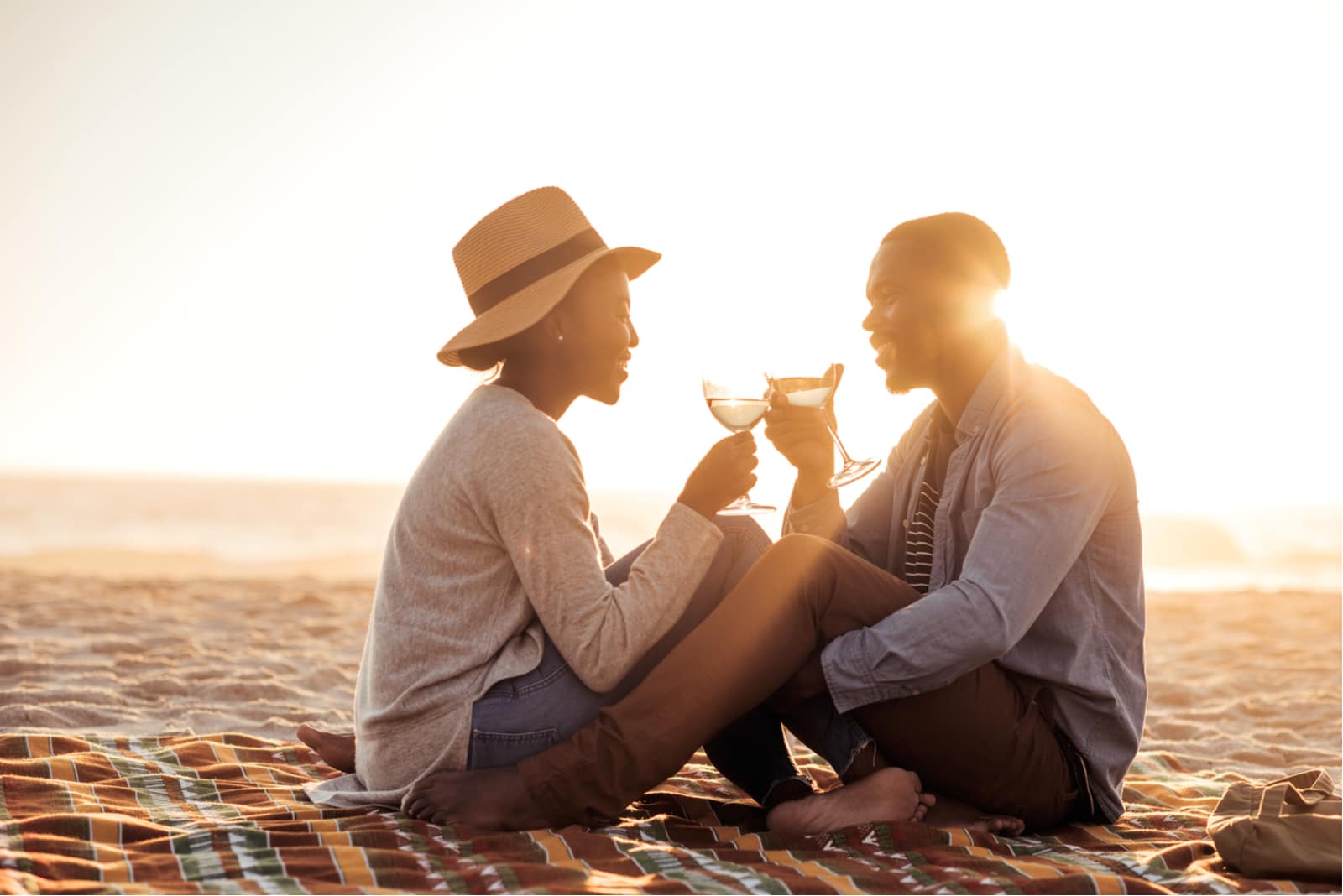 una romantica coppia afroamericana al tramonto seduta sulla spiaggia a bere vino