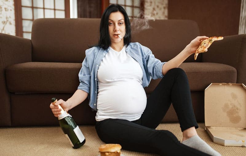 donna incinta alcolizzata che trasporta una bottiglia di pizza mentre fuma sul pavimento