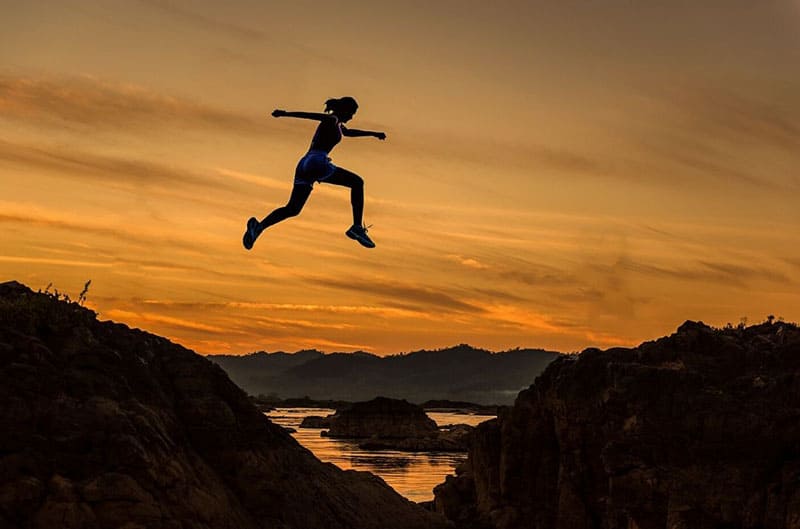 athletic girl jumping in between two mountains in silhouette