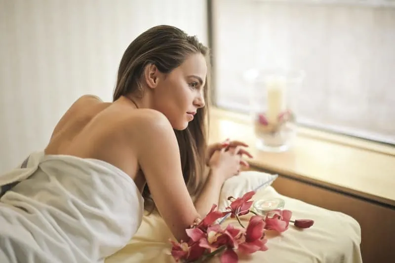 back view photo of woman in towel with flower and candles and window near her