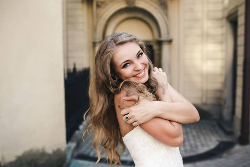 mulher bonita abraça-se a si própria, sorrindo, com um vestido branco