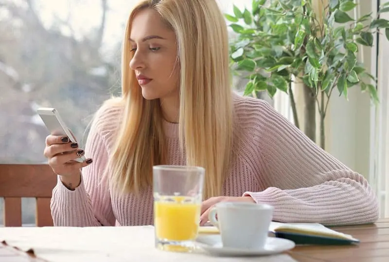 blonde woman texting while having tea and juice on table