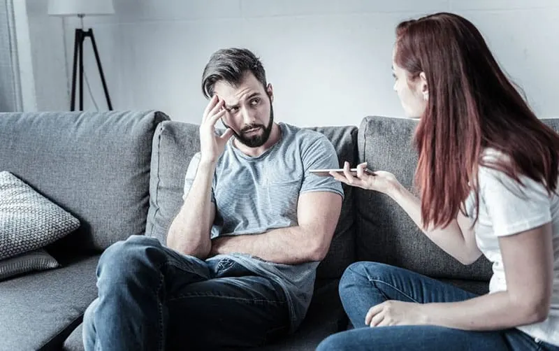 couple arguing on sofa while woman holding a cellphone