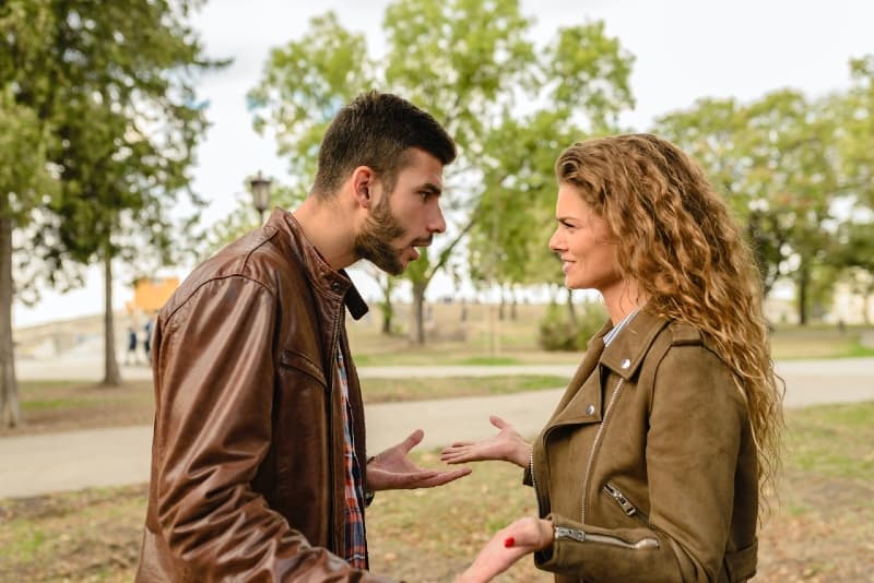 homem com casaco de cabedal castanho e mulher a discutir ao ar livre