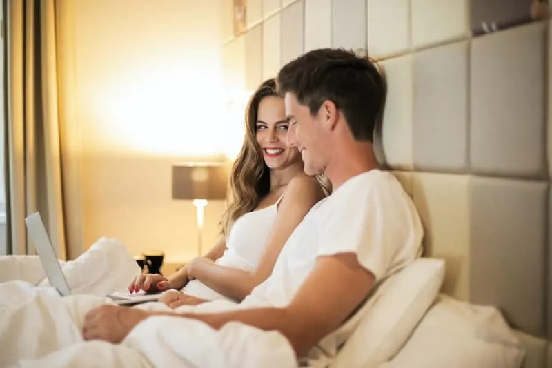 woman and man browsing laptop while sitting on bed