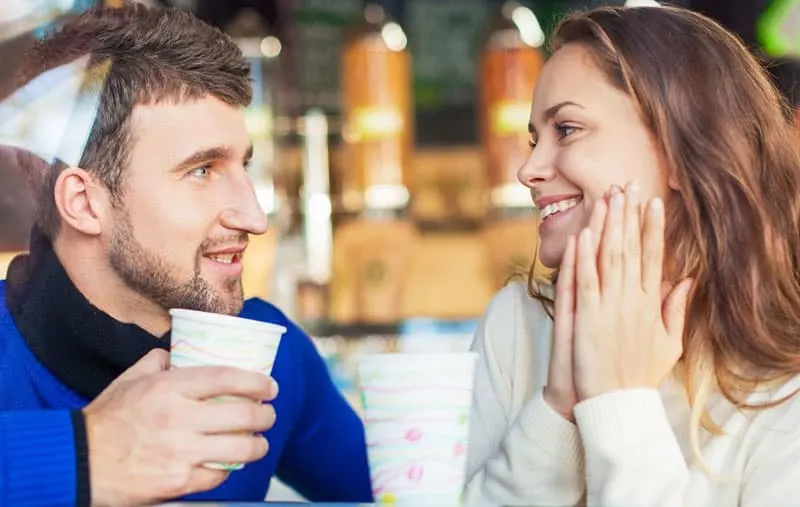 couple communicating in cafe with man holding cup and woman giggles