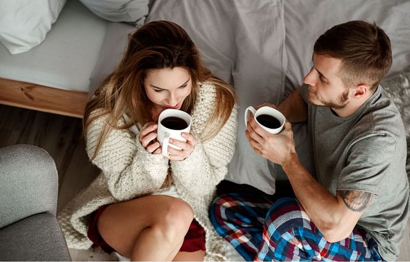 couple having coffee inside the bedroom sitting on the floor near the bed