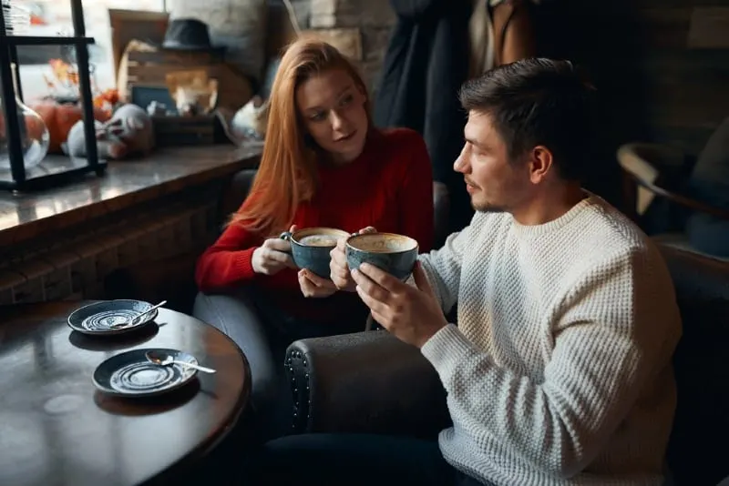 woman in red sweater and man holding cups of coffee