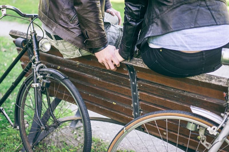 couple holding hands after a riding a bike sitting on the top of the bench