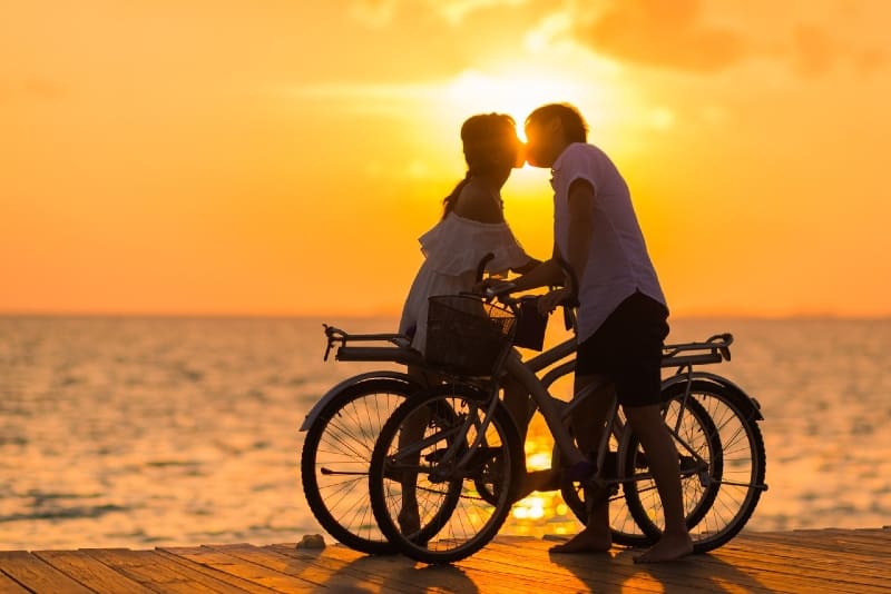 man and woman kissing on dock while holding bicycles