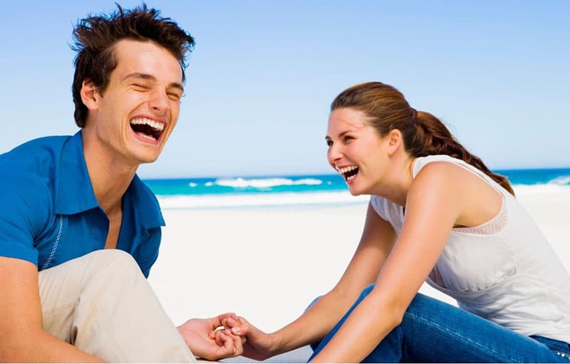 couple laughing in the beach both wearing blue and white tops and pants