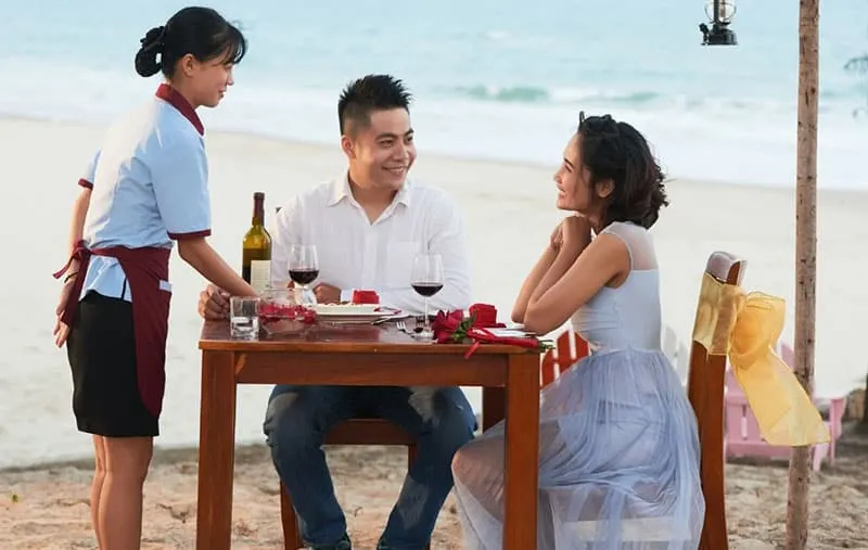 couple lunchdate by the beach with a waitress serving them