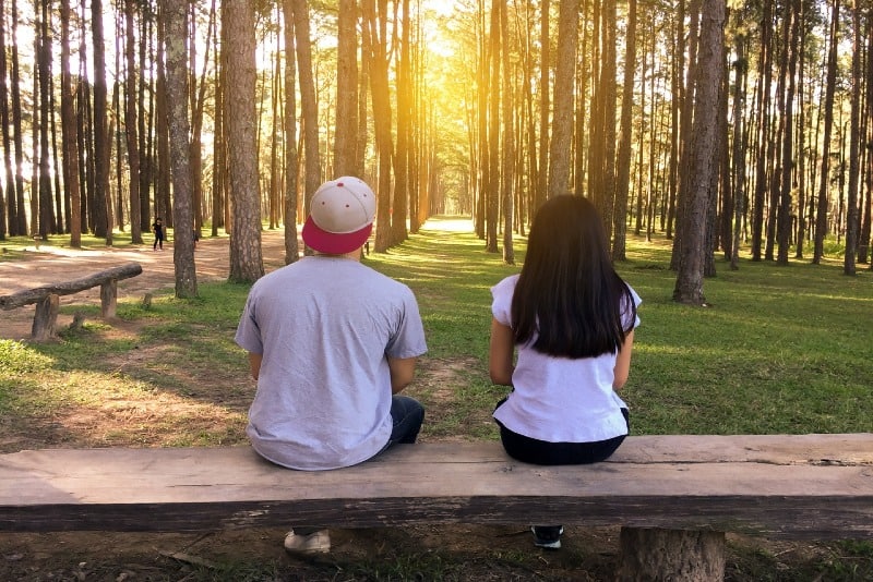 man and woman sitting on wooden bench in woods