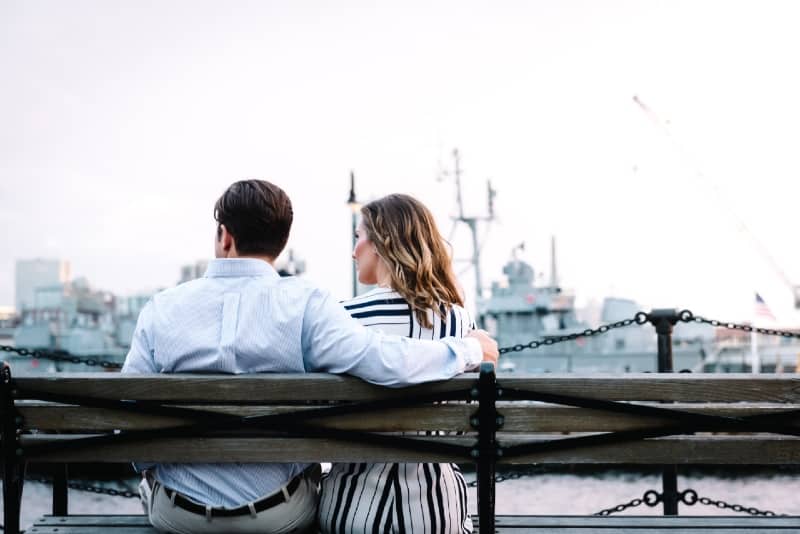 man and woman sitting on bench looking at water
