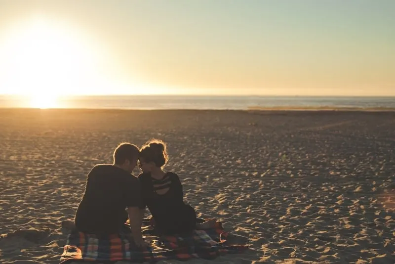 man and woman sitting on blanket on beach during sunset