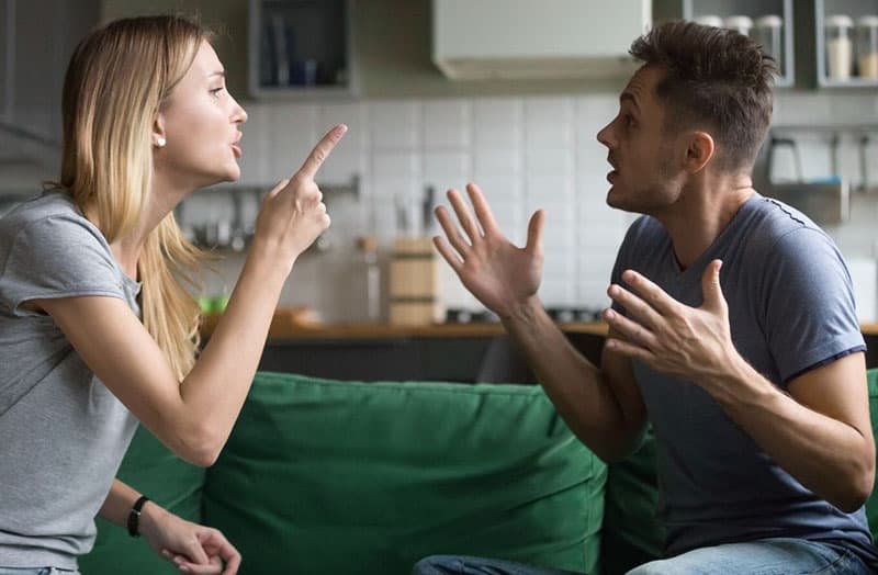 couple sitting on green sofa while arguing near kitchen