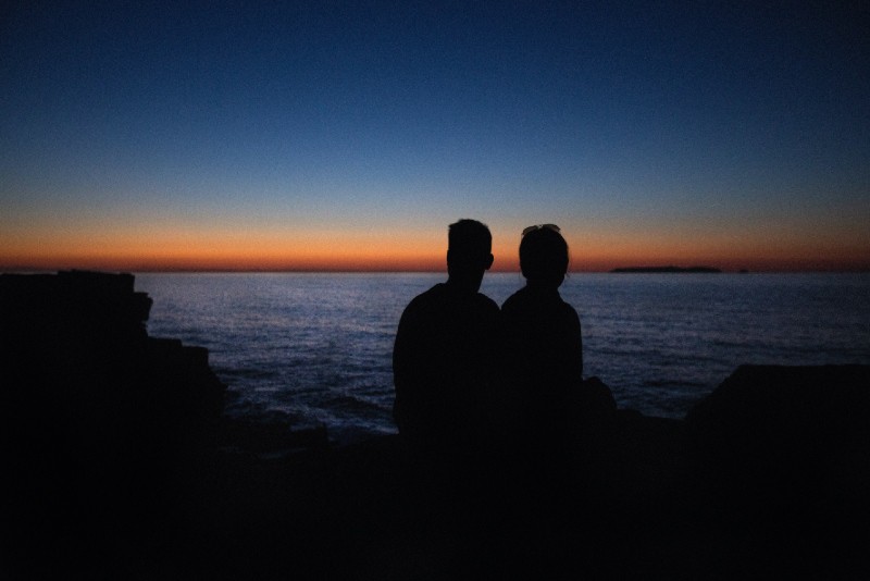 uomo e donna seduti su una roccia che guardano il mare