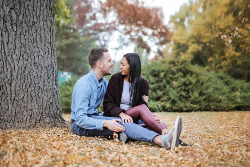 uomo e donna seduti sulle foglie sotto l'albero