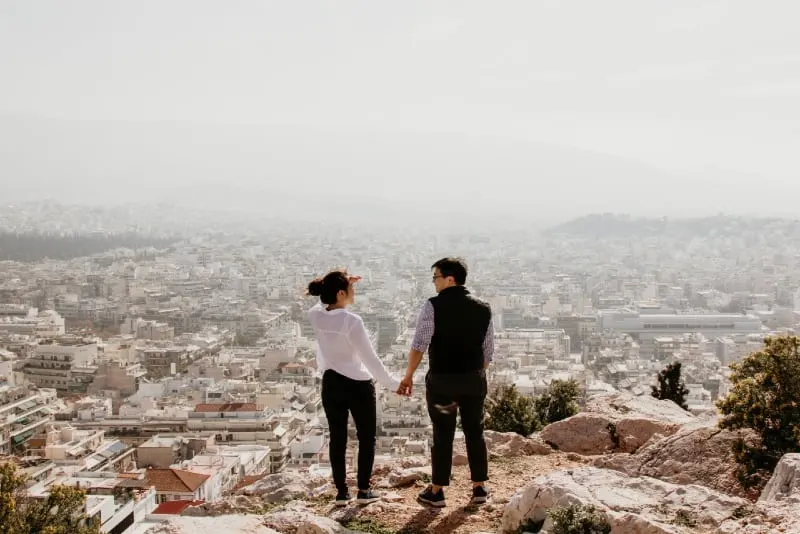 man and woman holding hands standing on top of cliff