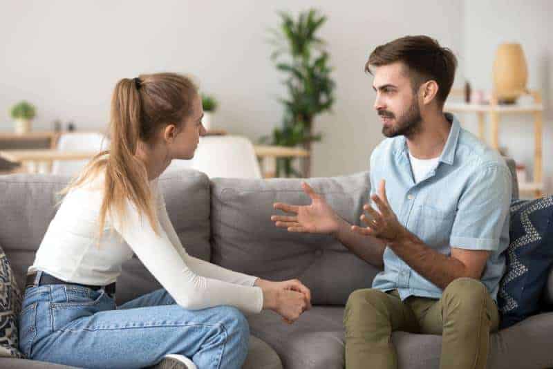 Sad man and woman couple talking while sitting on sofa