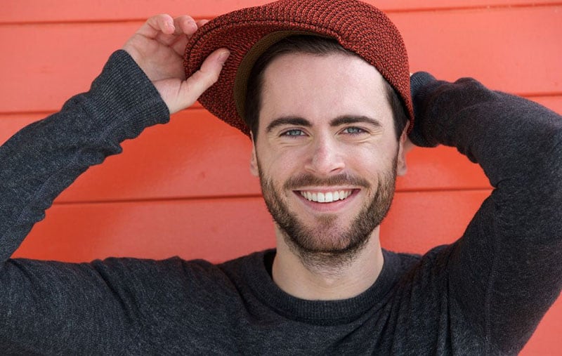 un bel ragazzo con la barba che tiene il suo cappello