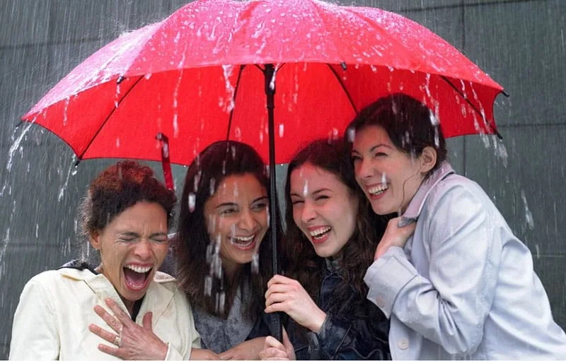 four women sharing under a red umbrella on a rainy day
