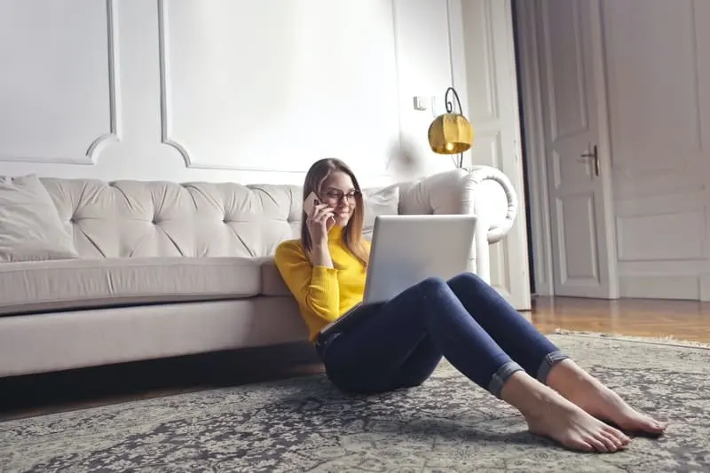 happy woman talking on phone with laptop sitting on the floor
