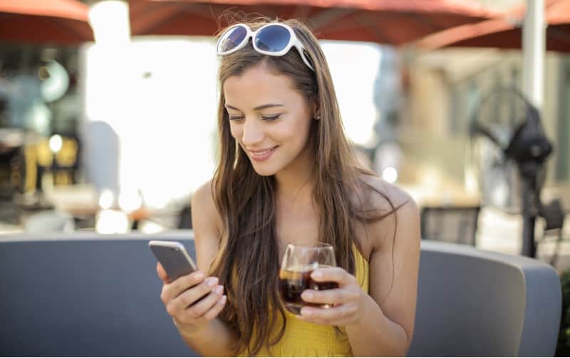 Donna felice che messaggia sul suo telefono con il bicchiere di vino nella mano opposta