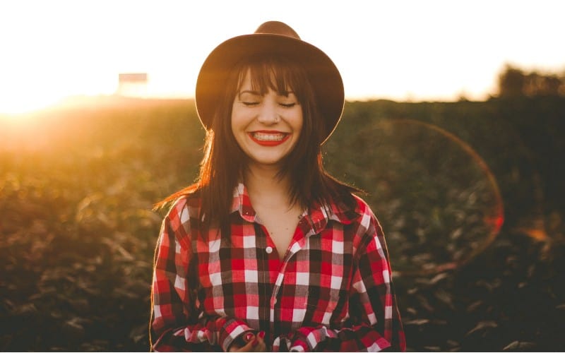 Happy woman with black hat on a field at sunset