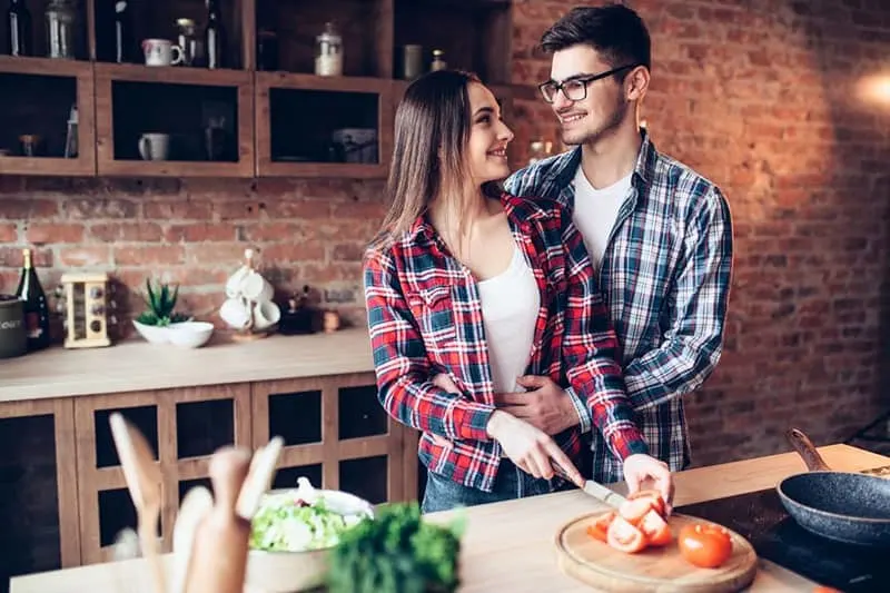 husband hugs wife while she is preparing fresh salad in the kitchen