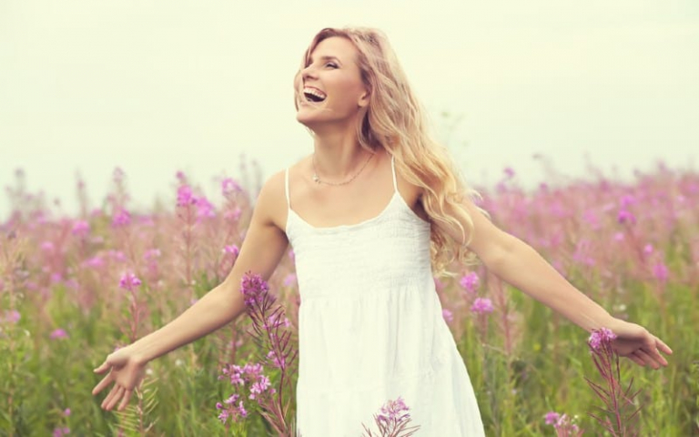 Happy woman in white dress on a field with flowers