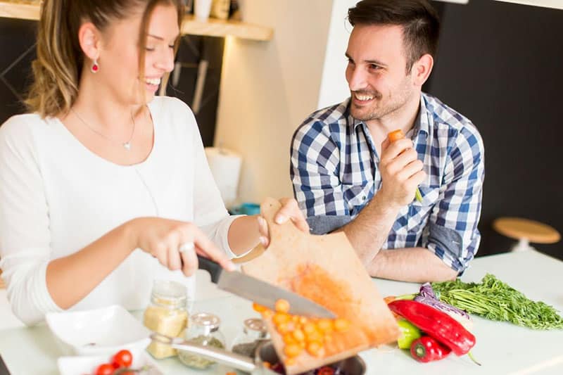 hombre y mujer cocinando con mujer sosteniendo cuchillo vertiendo verduras