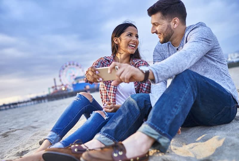 uomo e donna che si fanno un selfie in spiaggia 