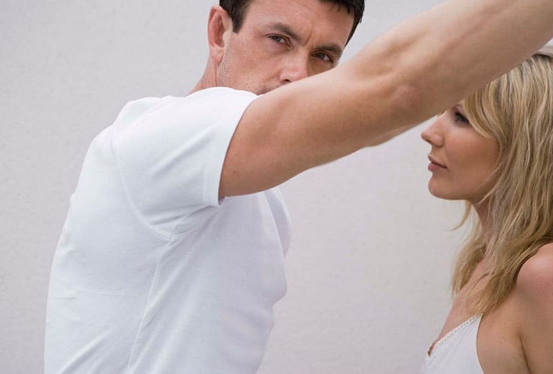 man and woman in white tops with guys hand on the wall where woman leans