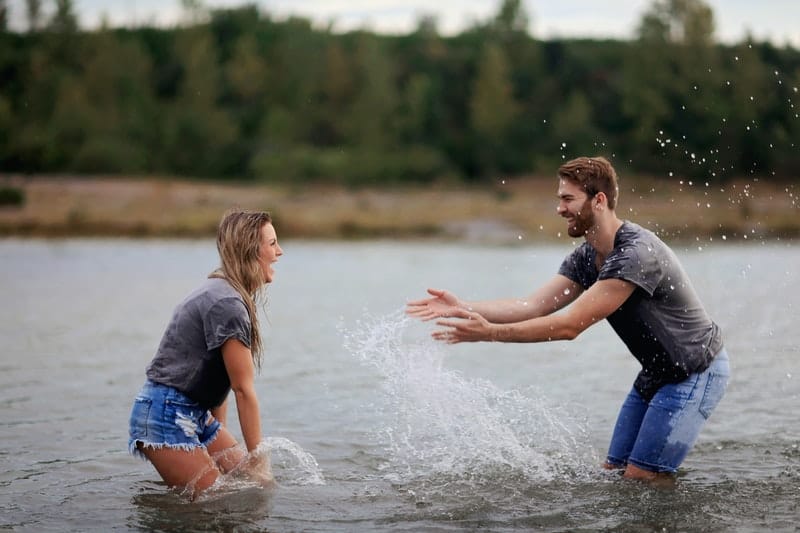 man and woman playing in a body of water wearing gray top and denim shorts