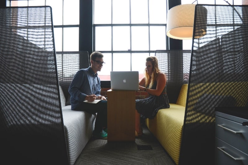 man and woman sitting on sofa looking at silver macbook